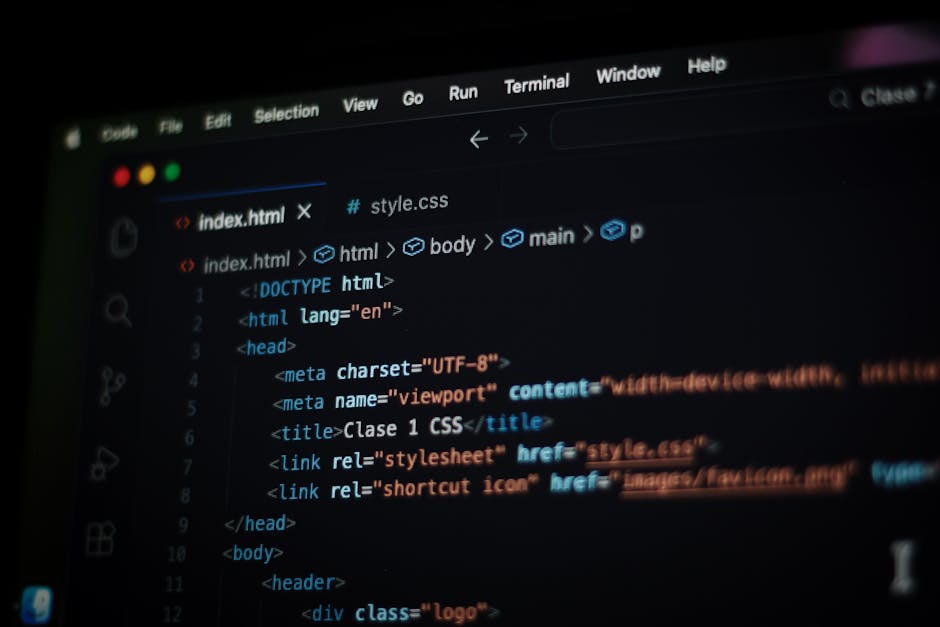 Close-up of a person's hands typing on a MacBook laptop placed on a dark table, displaying a coding interface with lines of code and commands visible on the screen. The background shows a dimly lit in