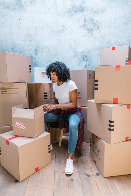 Close-up view of two cardboard moving boxes placed on a wooden floor inside a property, prepared for a home relocation. The upper box has the handwritten label 'STUFF' in red marker, accompanied by a